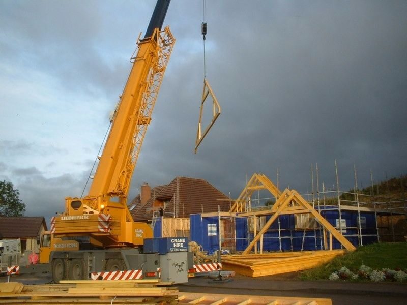 Crane lifting roof trusses onto a timber frame new build